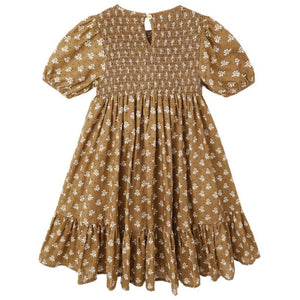 The Girls' Lydia Dress by Rylee & Cru is a brown, knee-length smocked dress with short sleeves, a white floral pattern, ruffled hem, and button closure at the back.