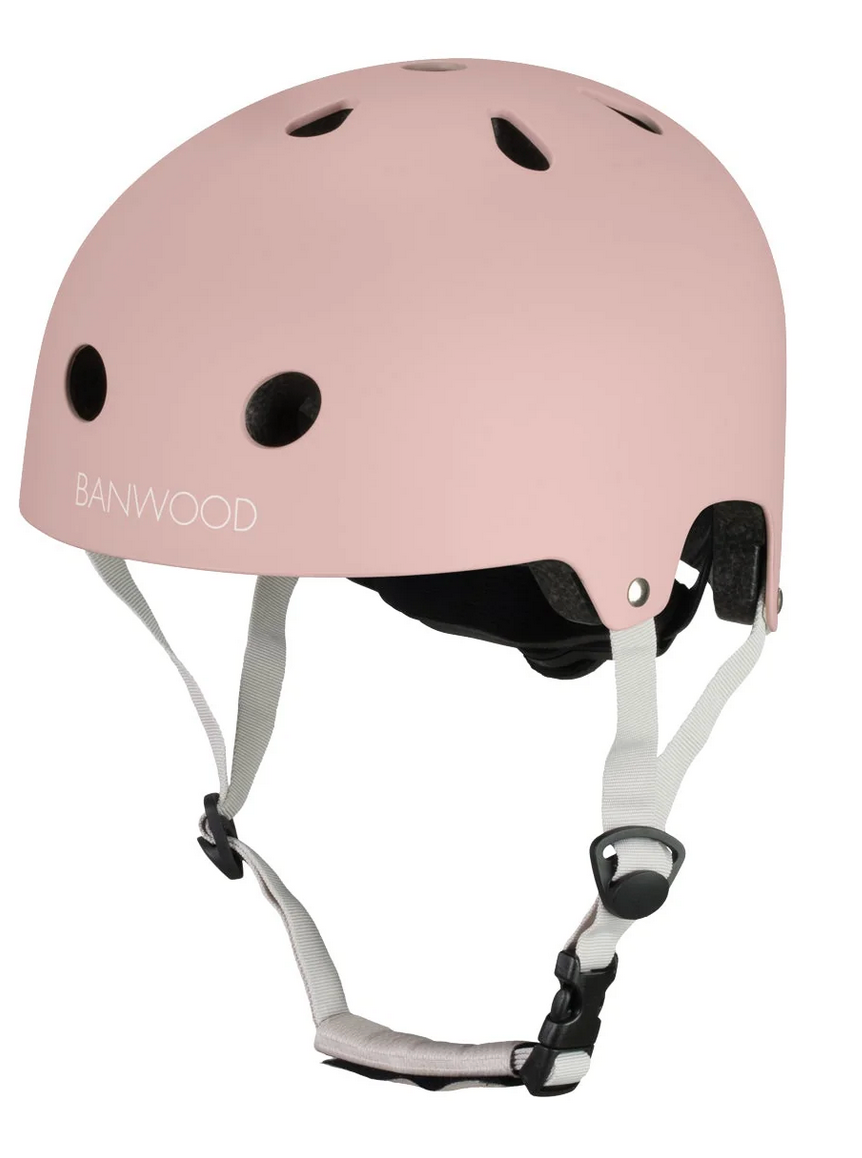 The Banwood Eco Helmet is a light pink helmet from the eco collection, featuring ventilation holes, white adjustable straps, a black buckle, and is crafted from recycled materials for a classic look.