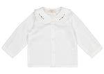 The Kidiwi Baby Girls' Hélena Blouse features off-white plumetis fabric, long sleeves, a ruffled Peter Pan collar with navy embroidery, and a button-down front with delicate decorative details.