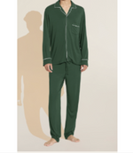 A person stands barefoot against a neutral background wearing the Eberjey Willam Long PJ Set, a matching men's dark green set with white piping, crafted from temperature-regulating TENCEL™ Modal fabric.