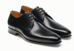 A pair of Magnanni Maddin Lace-Up black calfskin derby dress shoes with laces, low heels, and brown interiors from the Línea Flex collection, shown side by side on a white background.