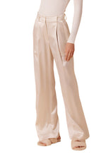 Someone dressed in Sablyn's Emerson Pleated Silk Pant, featuring a wide-leg and high-waist with a professional cut, paired effortlessly with a fitted long-sleeve top and fuzzy slippers.