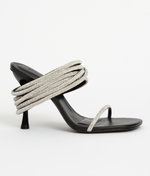 The Simkhai Infinity Crystal Strap Siren Sandal features a black high heel, thin toe strap, and multiple coiled crystal-embellished straps, perfect for evening wear and shown against a plain white background.