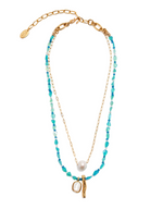 The Miyako Necklace by Lizzie Fortunato features a gold chain with aquamarine beads, a freshwater pearl, a gold branch-shaped pendant, and an oval charm, shown on a white background.
