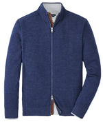 The Peter Millar Excursionist Flex Full-Zip Sweater in blue Merino wool, featuring a high collar, is shown flat on a white background with part of a checked shirt visible underneath.