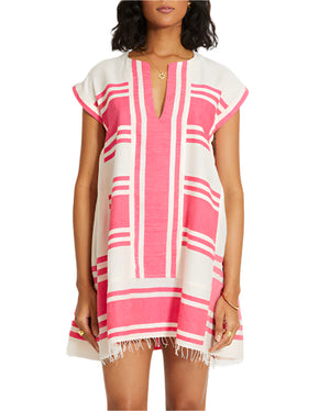 A woman wears the Lemlem Elina Caftan, a hand-woven cotton dress with short sleeves, pink geometric stripes, and a fringed hem.