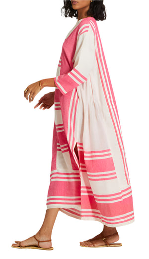 A woman models the Lemlem Fana Caftan—long, loose-fitting with pink and white stripes—paired with flat sandals and gold jewelry, walking sideways against a white backdrop for a look that's effortlessly versatile.