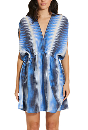A woman wears the Lemlem Alem Dress, a hand-spun cotton short dress with a sleeveless deep V-neck and vertical blue, white, and black stripes—ideal for resort wear.
