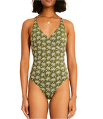 A woman showcases the Retiro One Piece swimsuit by Lemlem, featuring a stylish cross-back and V-neckline. The green jacquard design with a white palm tree pattern pops beautifully against the plain white background.