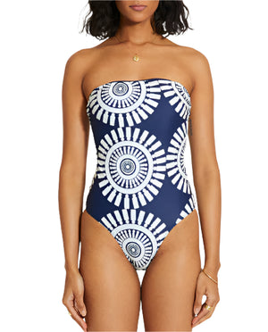 A woman wears the Lemlem Dinha One Piece, a strapless navy swimsuit featuring a white circular geometric pattern and a sleek neckline for a flattering look.