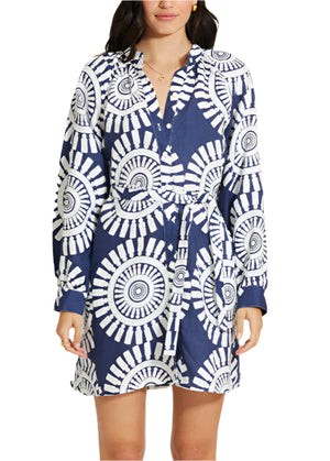 A woman wears the Lemlem Meaza Dress, a blue and white long-sleeve A-line dress with a bold circular pattern and matching waist tie.