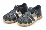 The Boys' Aiden Fisherman Sandal by L'Amour Shoes offers black leather sandals for children with a waxed finish, closed toes, buckle closure, and tan soles. These stylish and simple sandals are beautifully showcased on a white background.