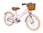 The Banwood Classic Children’s Bicycle is a light pink kids’ retro bike with tan tires, brown seat and handlebar grips, and a front wicker basket.