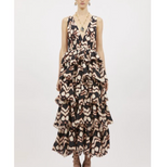 A woman wears the Ulla Johnson Dephne Dress—a sleeveless, V-neck silk taffeta maxi with black, beige, and blush abstract patterns and tiered silhouette—paired with ankle boots.