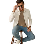 A man sits on a wooden stool, smiling and holding his sunglasses, dressed in the Faherty Legend™ Sweater Shirt layered over a tan tee with blue jeans.