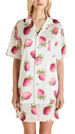 A person elegantly wears the Emeli Silk Pajamas by Olivia von Halle, showcasing a delightful pink strawberry print on a crisp white background, reminiscent of English tea parties.