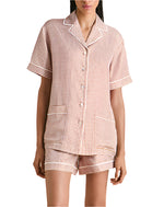 A person wears Olivia von Halle's Ingo Silk Pajamas—a short-sleeve button-up shirt and shorts—featuring a subtle, modern geometric motif in light colors.