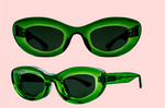 Two pairs of Thierry Lasry Jazz Sunglasses with green oval frames and dark lenses are displayed from front and side views against a light pink background.