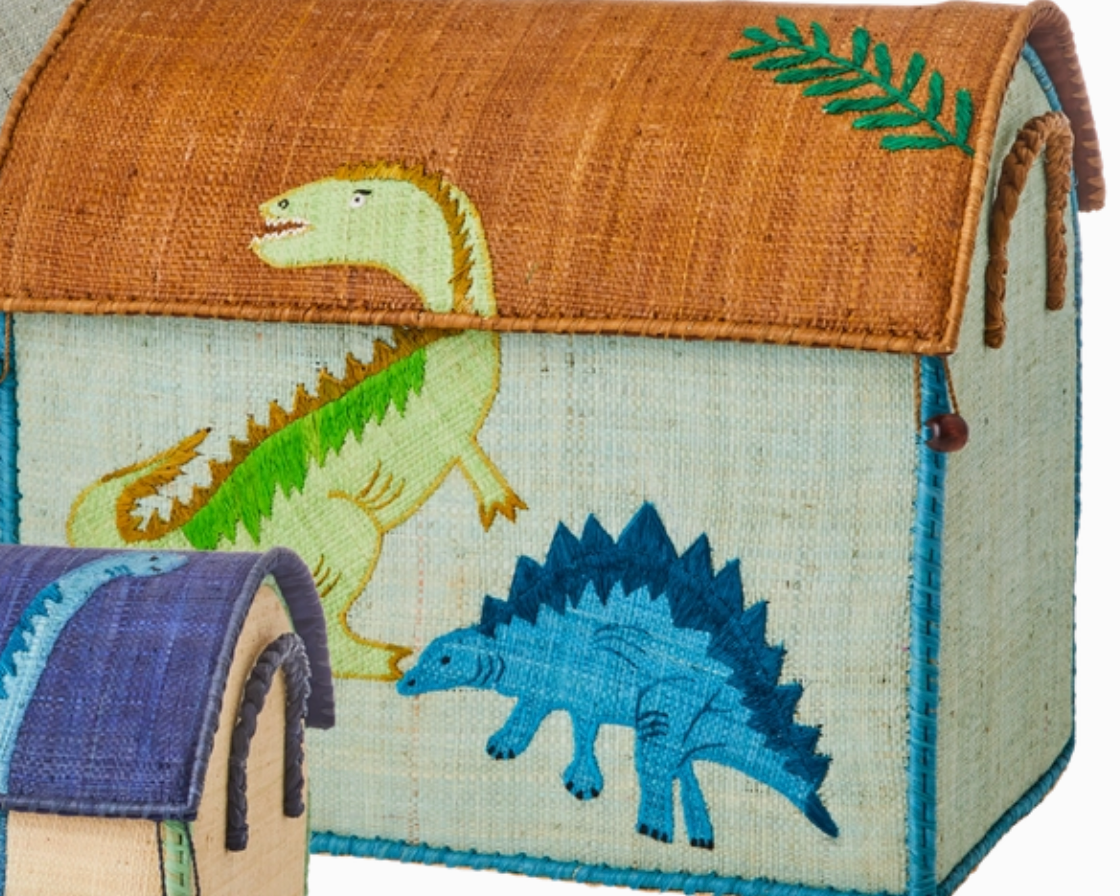 The Rice Raffia Toy Basket features a green dinosaur on the lid and a blue stegosaurus on the side, adding playful charm. A smaller matching basket is partially visible, perfect for fun and practical storage.