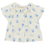 The Arsene & Les Pipelettes Baby Girls' Felixia Top is a white short-sleeve blouse with a blue shell and wave print, ruffled collar, and front buttons.