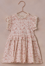 The Baby Girls' and Girls' Alice Dress by Noralee, featuring a pink floral pattern, ruffled sleeves, and embroidered lace trim, is elegantly displayed on a copper hanger against a soft beige background.