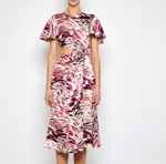 A woman wears the Prabal Gurung Flutter Slv Cut Out Dress, a short-sleeved, knee-length piece featuring a pink, red, black, and beige abstract pattern with a small side waist cutout.