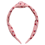 The Holly Headband from Pink Chicken showcases a pink fabric, a knotted top, and a lively floral pattern in red and dark blue.