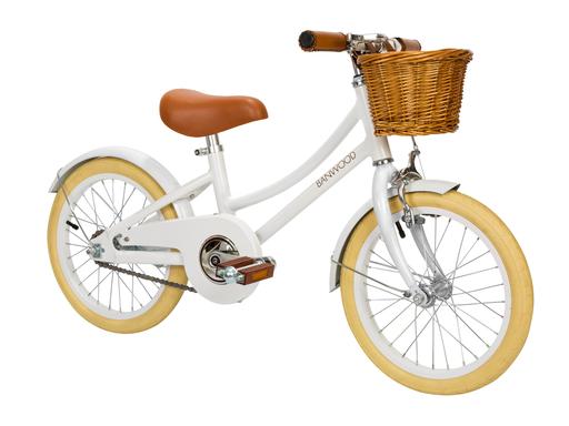 The Banwood Classic Children’s Bicycle features a white frame, tan tires, brown leather seat and handlebars, plus a cute wicker basket—ideal for stylish young riders.