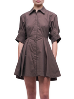 A person wears the Simkhai Jazzie Mini Dress—a brown, collared, short-sleeve, button-down dress with a flared skirt in crisp cotton poplin—standing against a plain light background.