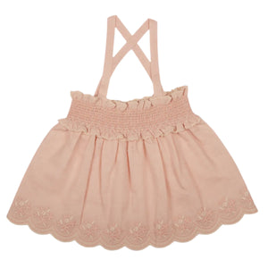 The Girls' Olivia Blouse by Early Sunday is a pink children's dress made from a cotton-linen blend, featuring cross-back straps, a smocked bodice, and floral embroidery along the scalloped hem.