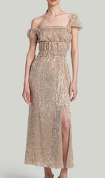 A woman models the Altuzarra Lily Dress, a gold off-the-shoulder gown with sequins, ruffles, and a thigh-high slit, standing against a simple background.