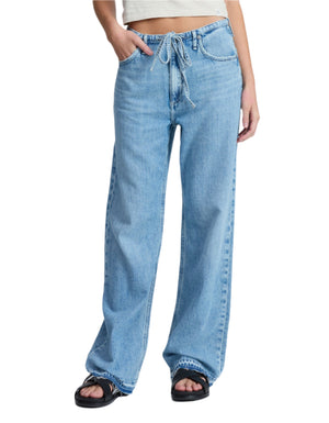 A person wears the Rag & Bone Ultra Featherweight Phoebe Drawstring Jean in light indigo with a drawstring waist, paired with a light crop top and black sandals, standing against a plain white background.