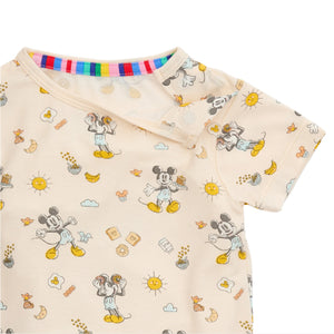 The beige shirt from Magnetic Me's "Mickey's Brunch Bunch" PJ set for kids is made of TENCEL™ modal and features a colorful collar with Mickey Mouse, sun, and food patterns.