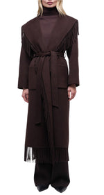 A person wearing the Simkhai Carrie Fringe Robe Coat—a long, dark brown shawl-collar style with a self-tie belt and fringed hem—over a matching turtleneck and wide-leg pants, standing against a white background.