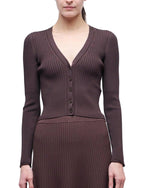 A woman models the Ailany Cardigan by Simkhai, a long-sleeved ribbed knit button-front piece paired with a matching brown skirt, shown from the front against a white background.