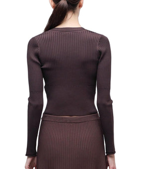 A woman with long brown hair in a ponytail is shown from the back wearing the Simkhai Ailany Cardigan, a ribbed knit, button-front style, paired with a matching skirt.