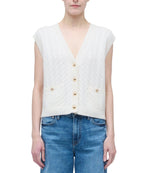 A person wearing the Simkhai Perrie Vest, a sleeveless white cable-knit cashmere V-neck with two front pockets, paired with blue jeans.
