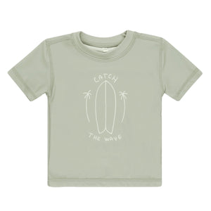 The Rylee & Cru Baby and Kids' Short-Sleeve Rashguard in light green features a white line surfboard and palm tree design with "Catch the Wave"—ideal for fun at the beach.