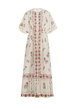 The Gesto Dress by Agua By Aguabendita is a long cream linen kaftan with wide short sleeves, featuring pink and green floral patterns and geometric borders on the front, hem, and sleeves.