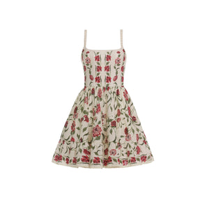 The Granadilla Dress by Agua By Aguabendita is a sleeveless, knee-length mini dress featuring a fitted bodice, square neckline, flared gathered skirt, and cream fabric with a red floral and green leaf print.