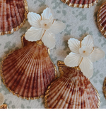 La Mer Shell Earrings from Collected By Farrell feature assorted brown seashells, mother of pearl, gold accents, and carved flower decorations on a spotted fabric background.