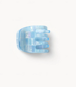 A blue, transparent Mini Claw from Machete, featuring a checkered pattern and crafted from Italian bio-acetate, is set against a white background.
