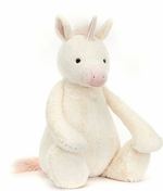 Introducing the Bashful Unicorn, Giant by Jellycat: a plush toy with vanilla fur, featuring a light pink horn and enchanting black eyes, seated upright. It also has pink accents on its ears and tail.