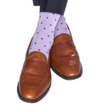 A person is shown from the knees down against a white background, wearing dark pants, brown leather loafers, and Dapper Classics’ Dot Mid Calf Socks in light purple with small dark polka dots.