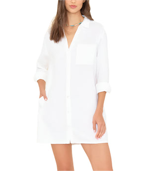 A woman wearing the Tyson Dress by Xirena, a loose cotton gauze mini shirtdress with long sleeves, chest pocket, button front, and rolled cuffs.