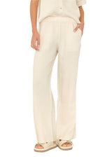 Person wearing Xirena Romany Pant—cream-colored, lightweight linen pull-on pants with elastic waist—paired with a matching short-sleeve top and beige platform sandals; one hand in pocket, shown from shoulders down.