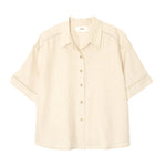 The Xirena Hendry Shirt is a beige, short-sleeved linen button-up with coconut buttons and a collar, shown on a plain white background.