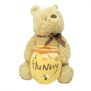 The Classic Pooh Waggie Musical by Kids Preferred is a plush bear holding a yellow "Hunny" pot with bee designs and wears a brown ribbon around its neck.