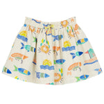 The Girls' Flavie Skirt by Arsene & Les Pipelettes is a white skirt with vibrant prints of fish, waves, suns, and oranges in blue, orange, yellow, and green. It features an elastic waistband for comfort and is perfect for girls who love colorful designs.