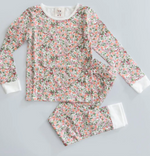 The Timo & Violet Kids' The Two Piece Pajamas, made from organic cotton, feature long sleeves, white cuffs, and a pink, green, and white floral pattern. Shown laid flat on a light gray surface.